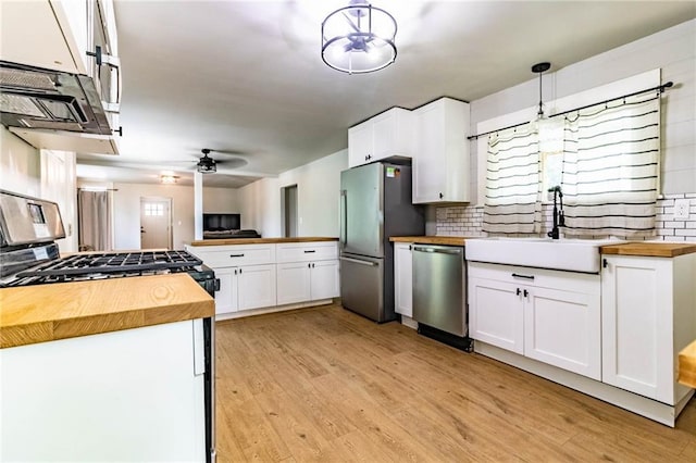 kitchen featuring butcher block counters, sink, decorative light fixtures, and white cabinetry