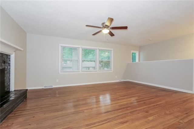 unfurnished living room featuring a brick fireplace, wood-type flooring, and ceiling fan