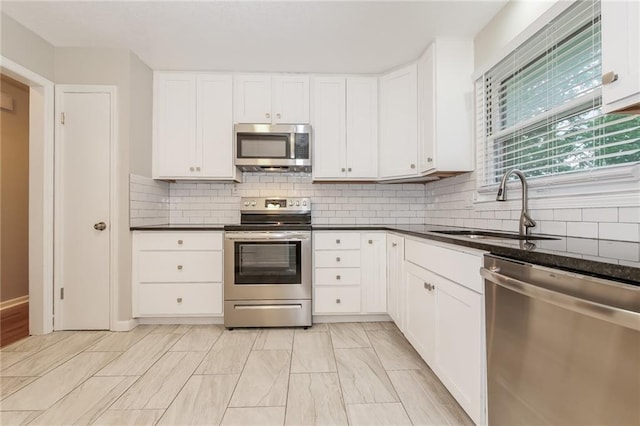 kitchen featuring appliances with stainless steel finishes, sink, backsplash, white cabinetry, and dark stone counters