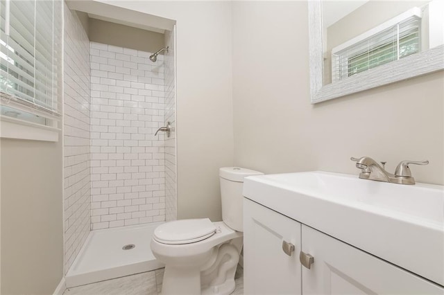 bathroom with a tile shower, toilet, and vanity