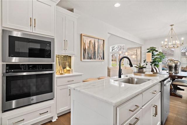 kitchen with a kitchen island with sink, a sink, white cabinets, appliances with stainless steel finishes, and tasteful backsplash