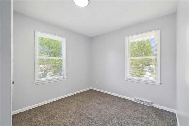 unfurnished room with baseboards, visible vents, and dark carpet