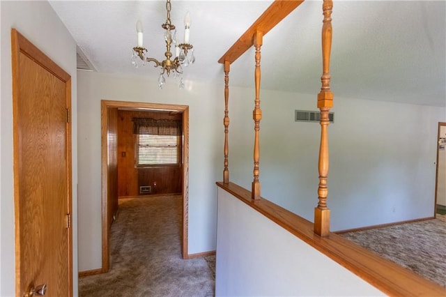 corridor with a notable chandelier and dark colored carpet