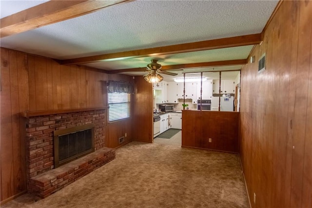 carpeted living room featuring a textured ceiling, wooden walls, beamed ceiling, ceiling fan, and a fireplace