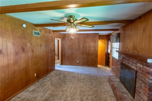 unfurnished living room with beamed ceiling, a brick fireplace, light carpet, and wood walls