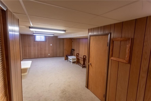 basement featuring light colored carpet, wooden walls, and a paneled ceiling