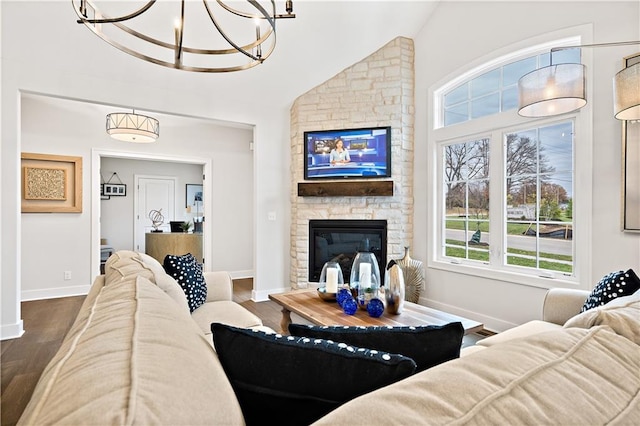 living room featuring wood-type flooring, a stone fireplace, vaulted ceiling, and a chandelier