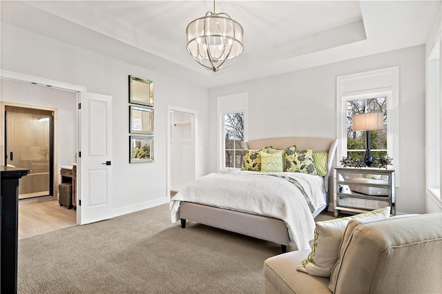 bedroom with an inviting chandelier, ensuite bathroom, a tray ceiling, and hardwood / wood-style flooring