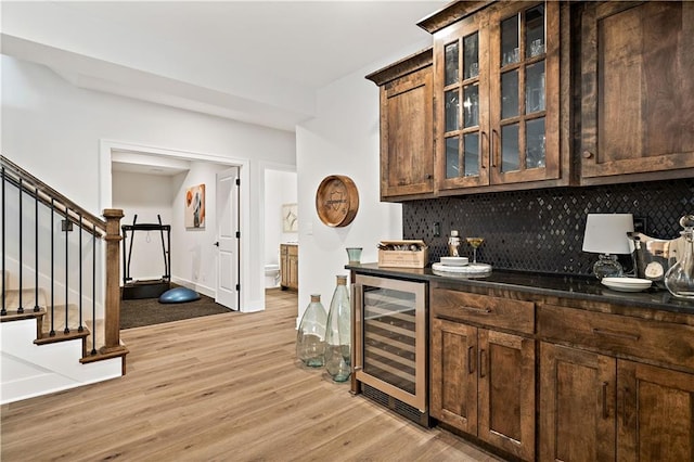 kitchen featuring dark stone countertops, light wood-type flooring, wine cooler, backsplash, and dark brown cabinetry