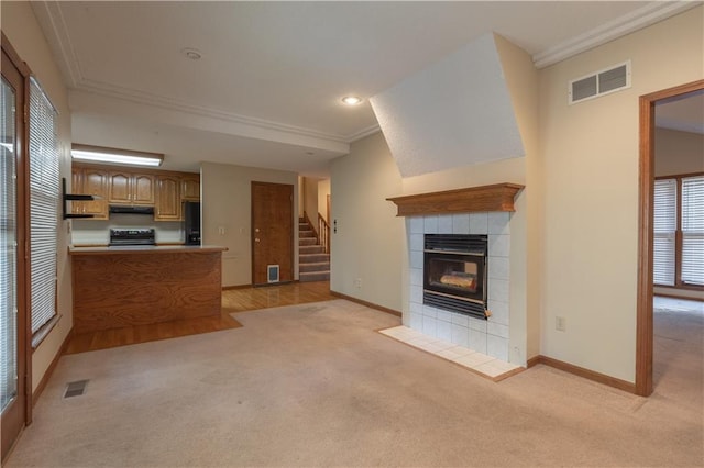 unfurnished living room with crown molding, a tiled fireplace, and light colored carpet