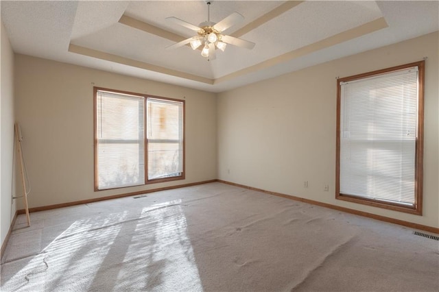 unfurnished room with ceiling fan, a raised ceiling, and light colored carpet