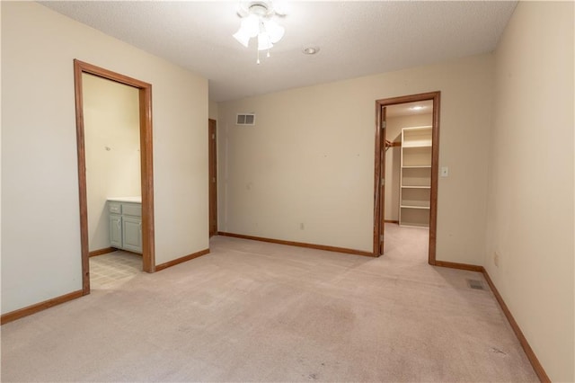 unfurnished bedroom featuring a spacious closet, ensuite bath, a closet, and light colored carpet