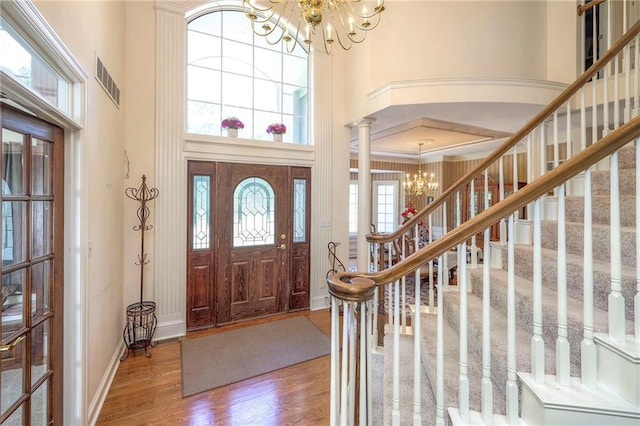 entrance foyer featuring a notable chandelier, a towering ceiling, hardwood / wood-style flooring, and ornate columns