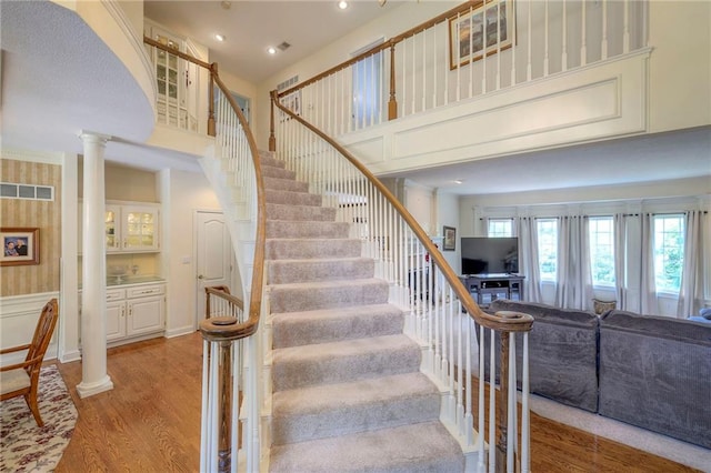 stairway featuring hardwood / wood-style floors, a high ceiling, and ornate columns