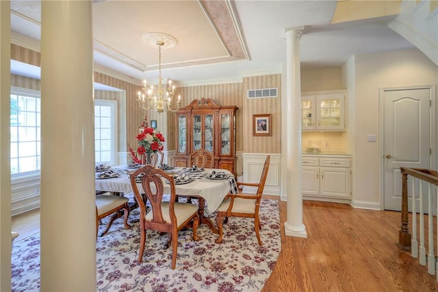 dining room with ornate columns, a chandelier, a tray ceiling, crown molding, and light hardwood / wood-style flooring