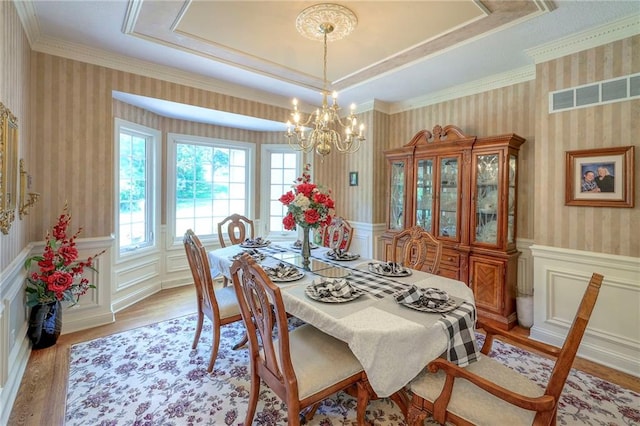 dining room with an inviting chandelier, light hardwood / wood-style floors, and a raised ceiling