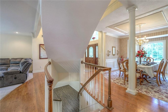 stairway featuring an inviting chandelier, wood-type flooring, crown molding, and decorative columns