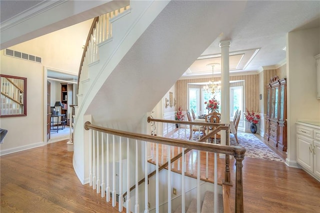 stairway with an inviting chandelier, ornamental molding, and hardwood / wood-style floors