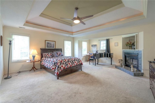 carpeted bedroom featuring a tray ceiling, a fireplace, ornamental molding, and ceiling fan