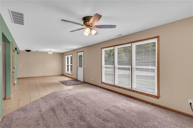 carpeted spare room featuring visible vents, baseboards, ceiling fan, and tile patterned flooring