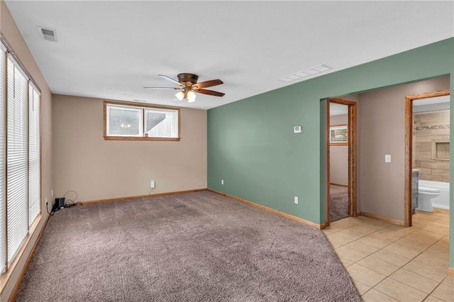 empty room featuring a ceiling fan, light tile patterned floors, light colored carpet, and visible vents