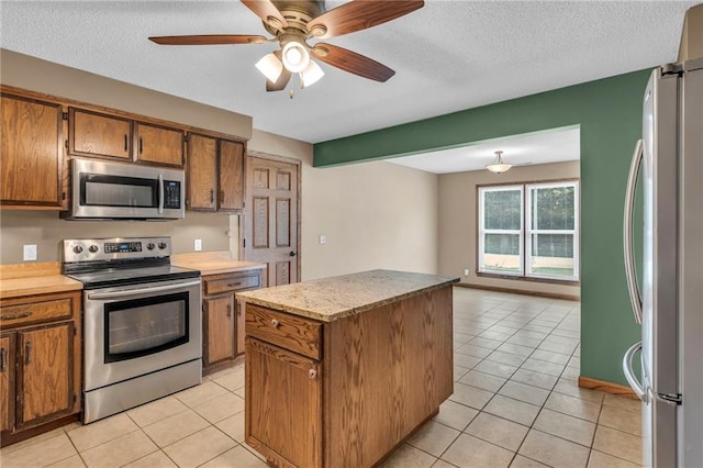 kitchen with a textured ceiling, light tile patterned flooring, brown cabinetry, and stainless steel appliances