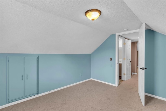 additional living space with light colored carpet, a textured ceiling, lofted ceiling, and baseboards