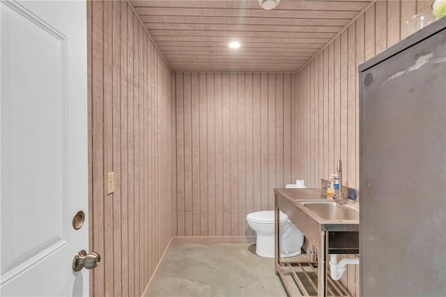 half bathroom featuring wooden walls, concrete floors, wood ceiling, toilet, and a sink