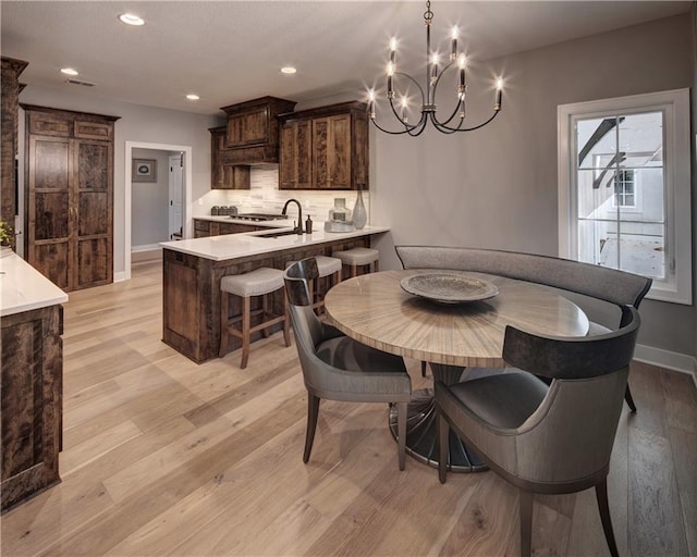 dining room featuring ceiling fan with notable chandelier, sink, and light wood-type flooring