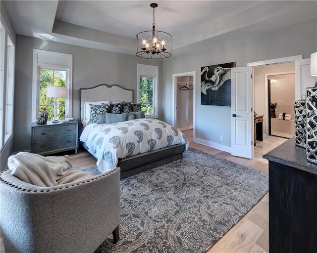 bedroom featuring a notable chandelier, multiple windows, a walk in closet, and a tray ceiling