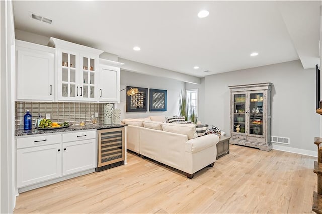 kitchen featuring white cabinetry, dark stone countertops, light wood-type flooring, wine cooler, and decorative backsplash