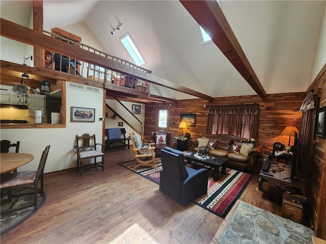 living room with a skylight, beamed ceiling, high vaulted ceiling, wood walls, and wood-type flooring