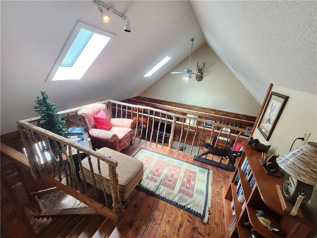 living area featuring hardwood / wood-style flooring, ceiling fan, lofted ceiling with skylight, and a textured ceiling