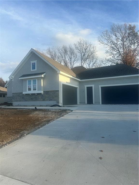 view of front of house featuring an attached garage, stone siding, concrete driveway, and stucco siding