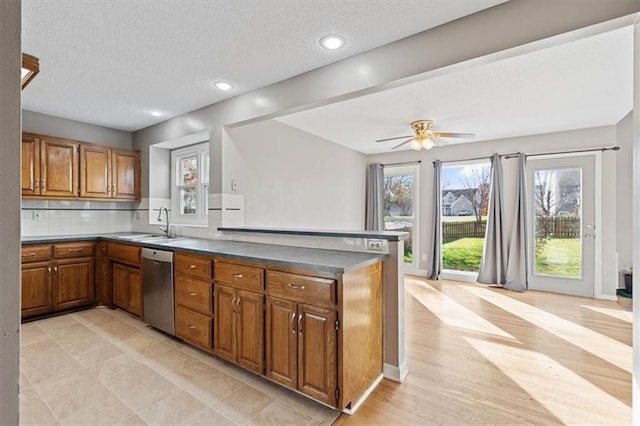 kitchen with kitchen peninsula, backsplash, stainless steel dishwasher, a textured ceiling, and sink