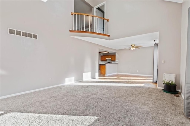 unfurnished living room with ceiling fan, carpet floors, and a high ceiling