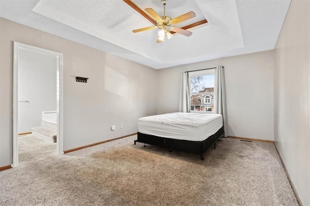 bedroom with a raised ceiling, ceiling fan, carpet flooring, and a textured ceiling