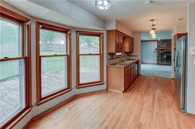 kitchen featuring pendant lighting, sink, stainless steel fridge, light hardwood / wood-style floors, and a brick fireplace