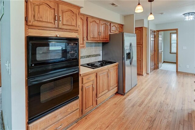 kitchen featuring backsplash, decorative light fixtures, light hardwood / wood-style flooring, and black appliances