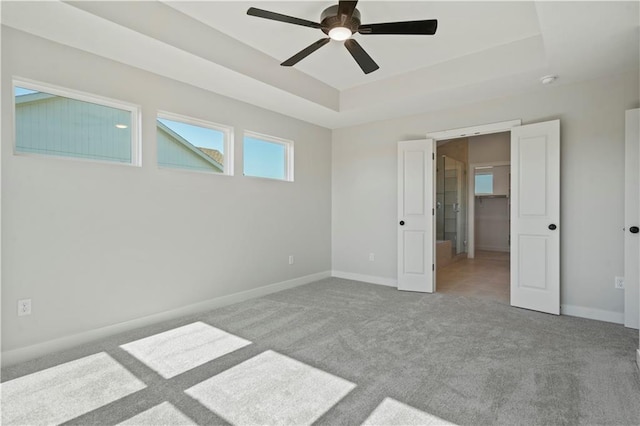 spare room with ceiling fan, a raised ceiling, and light carpet