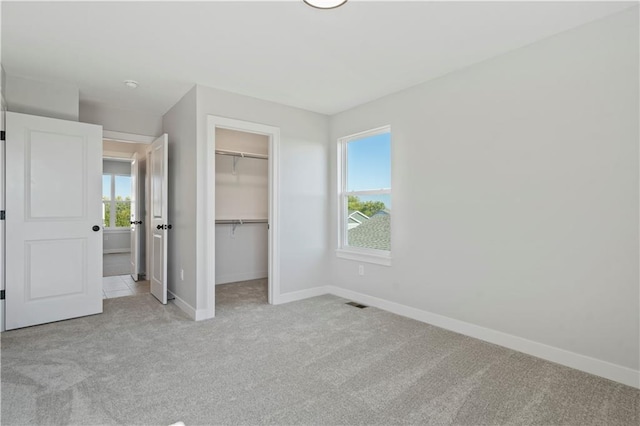 unfurnished bedroom featuring light carpet, a walk in closet, a closet, and multiple windows