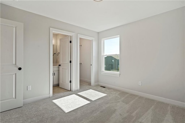 unfurnished bedroom featuring ensuite bath, a walk in closet, and light colored carpet