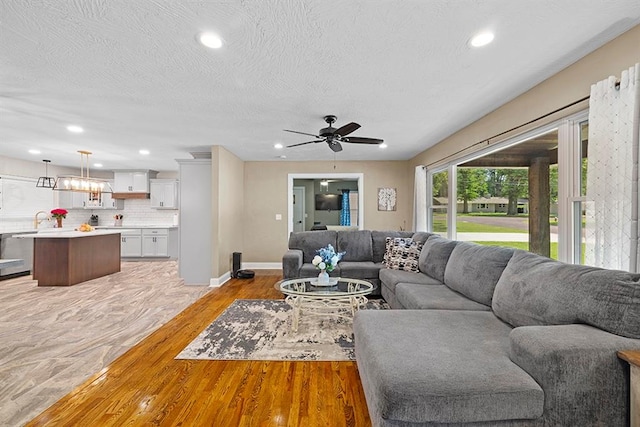 living room with sink, light hardwood / wood-style flooring, a textured ceiling, and ceiling fan