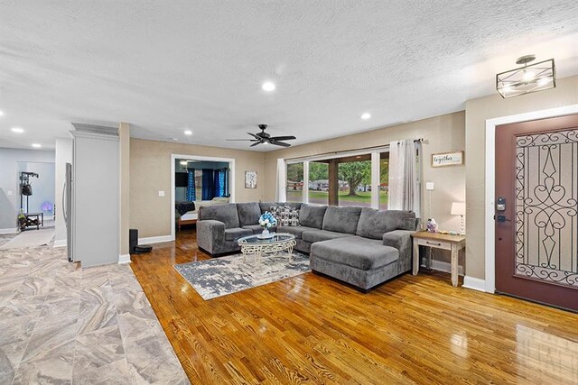 living room with ceiling fan, a textured ceiling, and light hardwood / wood-style flooring