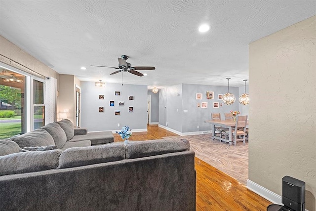 living room with light hardwood / wood-style floors, ceiling fan with notable chandelier, and a textured ceiling