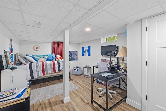 bedroom with light wood-type flooring and a drop ceiling