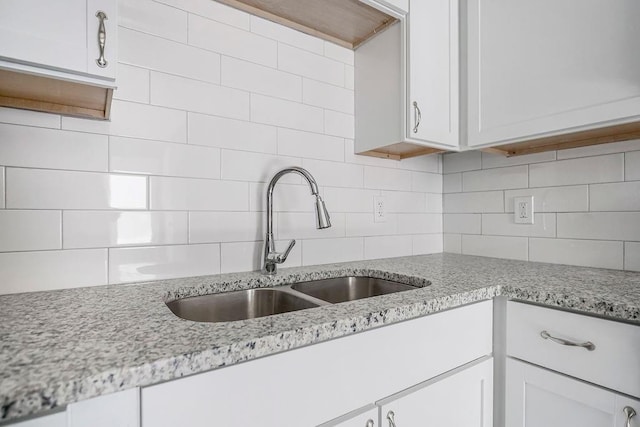 kitchen with tasteful backsplash, sink, white cabinetry, and light stone countertops