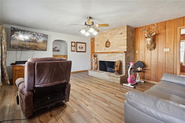 living room with wood walls, ceiling fan, light hardwood / wood-style floors, and a stone fireplace