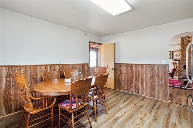 dining space featuring light wood-style floors, wooden walls, arched walkways, and wainscoting