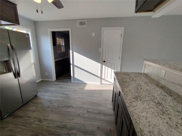 kitchen featuring stainless steel refrigerator with ice dispenser, wood-type flooring, ceiling fan, light stone counters, and dark brown cabinetry